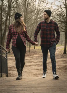 Plenerowa sesja ciążowa w Toruniu – para w dopasowanych koszulach w kratę spaceruje po parku – fot-city fotografia